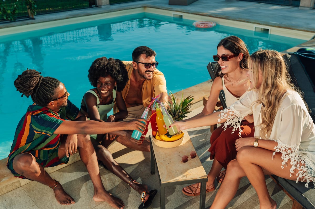 Group of diverse friends enjoying a vibrant summer day, toasting with colorful drinks by the poolside