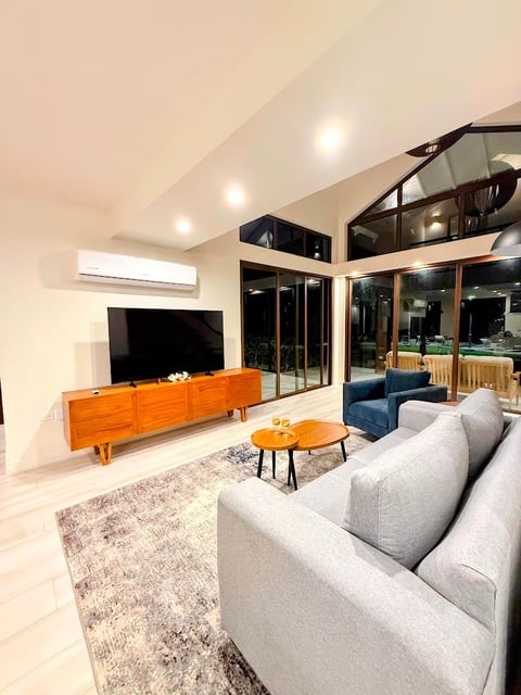 Modern living room with gray sofa, wood media console, TV, round wood table, and glass doors opening to outdoor deck