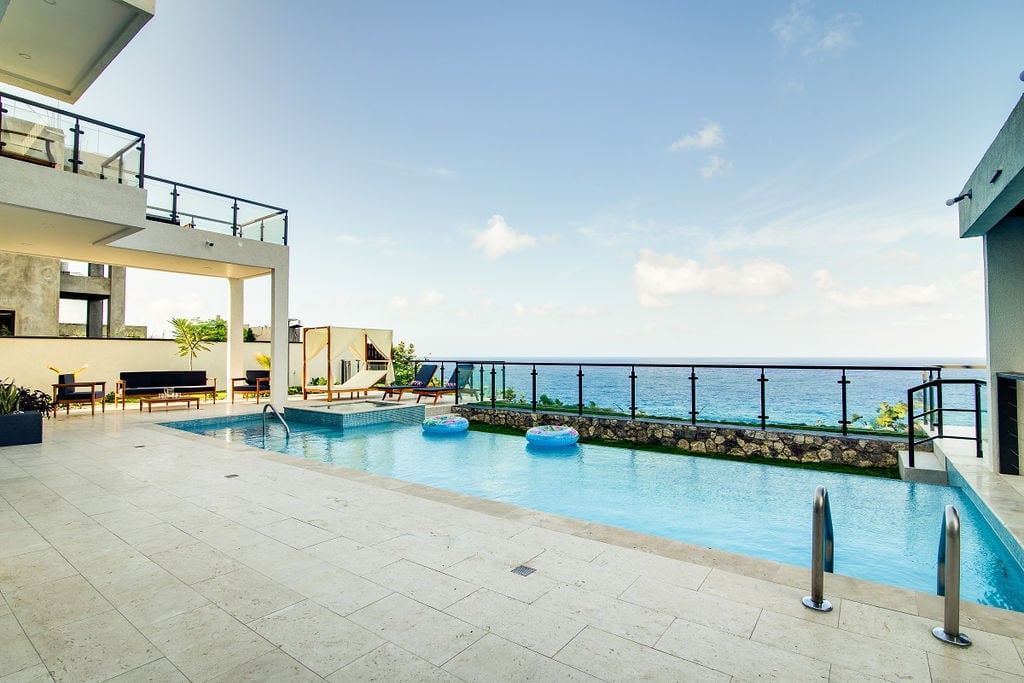Luxury beachfront resort with infinity pool overlooking the ocean, modern architecture, and lounging area on sunny day