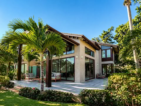 Modern residential home with concrete and wood exterior, large windows, surrounded by palm trees and manicured landscaping