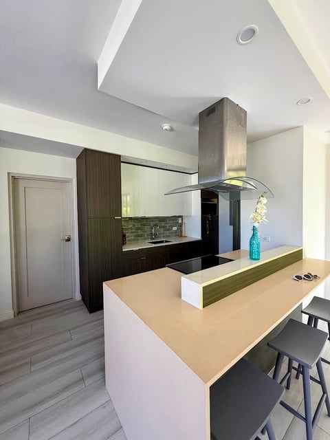 Modern kitchen with white island, dark cabinetry, stainless steel range hood, and black bar stools